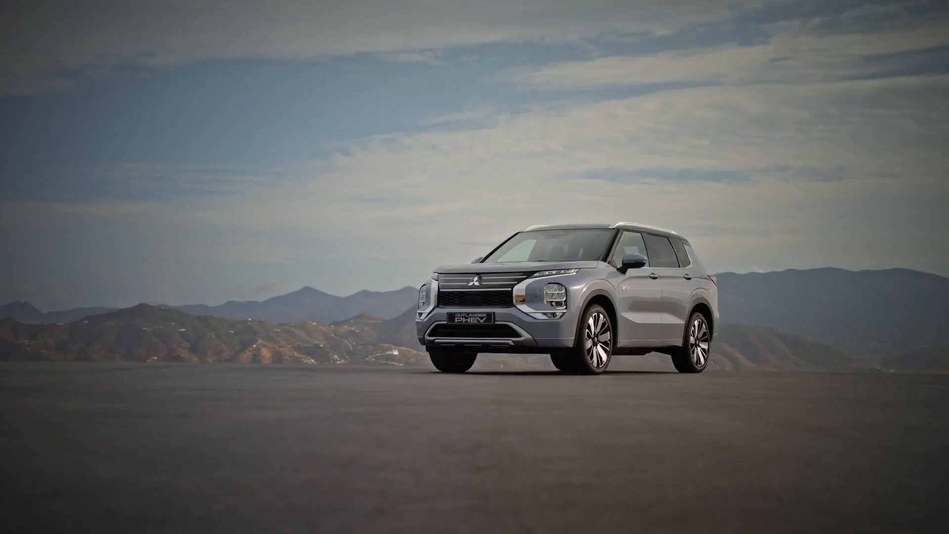 Mitsubishi Outlander PHEV cinzento de frente, a três quartos, num planalto com as serras ao fundo