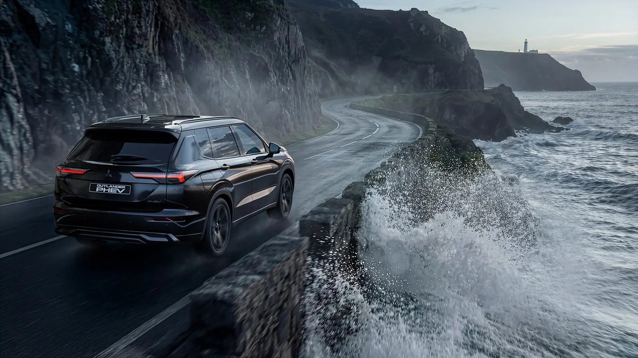 Outlander PHEV preto numa estrada de costa molhada, com as ondas a rebentar contra o muro