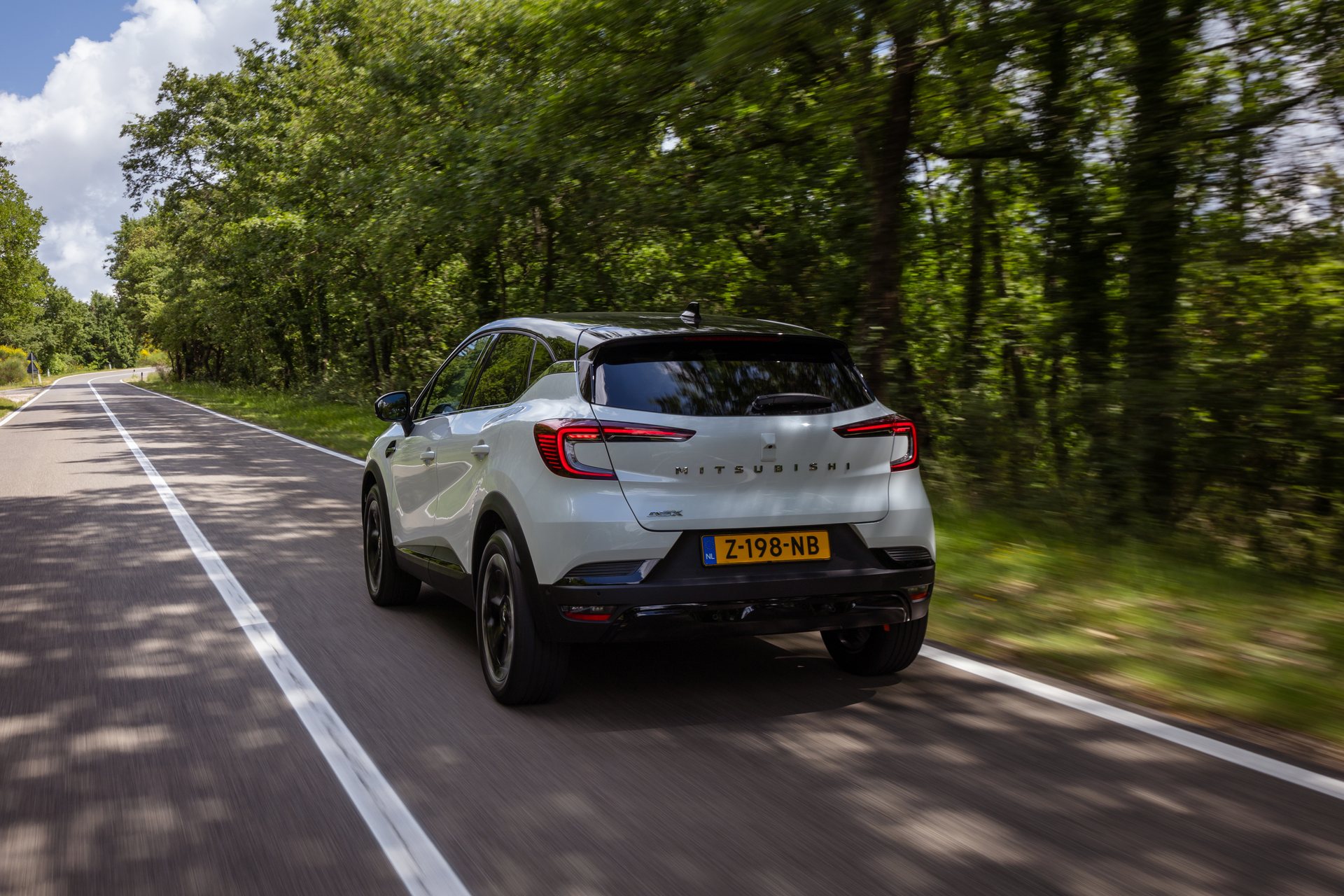 Mitsubishi ASX branco em andamento numa estrada ladeada de árvores, visto de trás