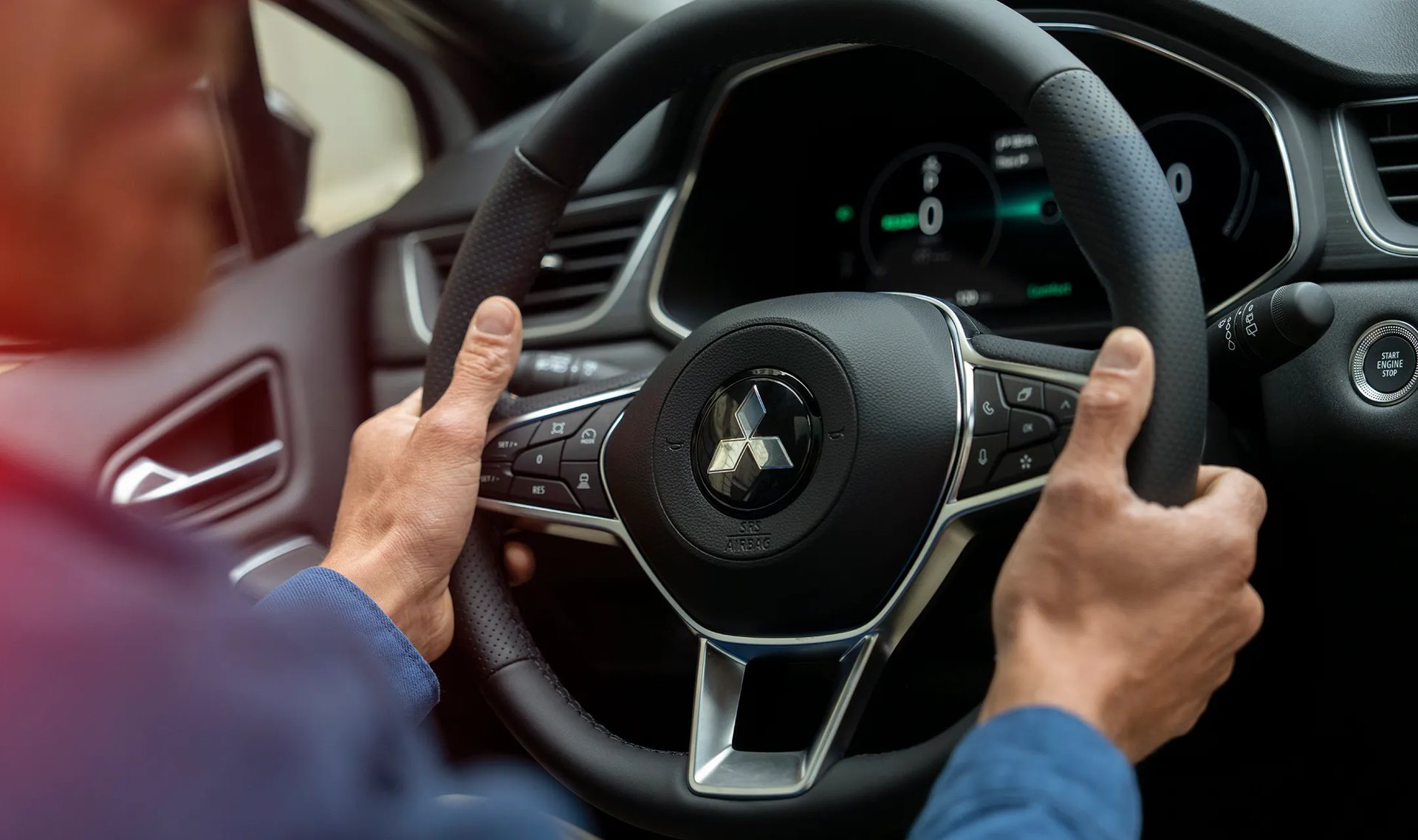 Mãos no volante do Mitsubishi Grandis, com as teclas de comando nos raios e o painel digital ao fundo