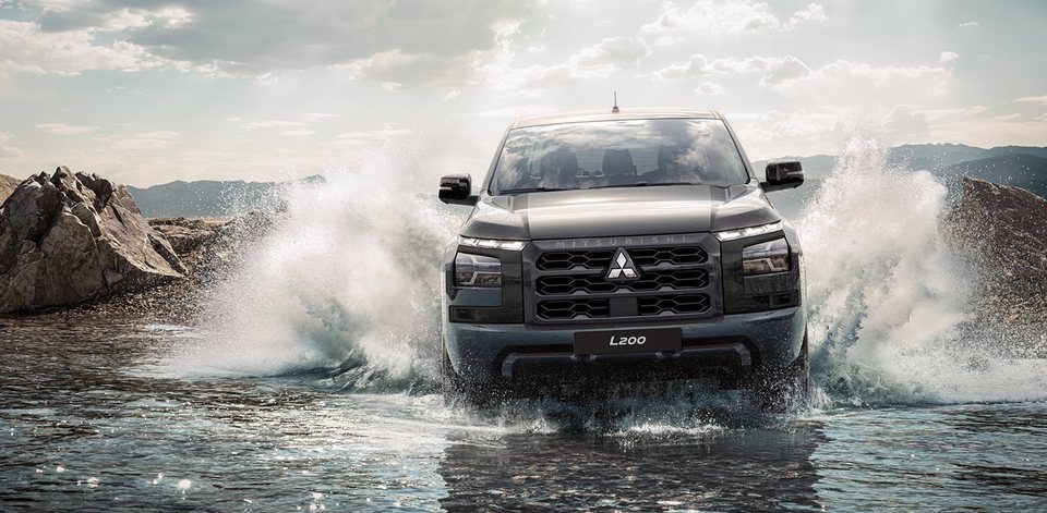 Mitsubishi L200 de frente a atravessar um rio, com a água a saltar dos dois lados