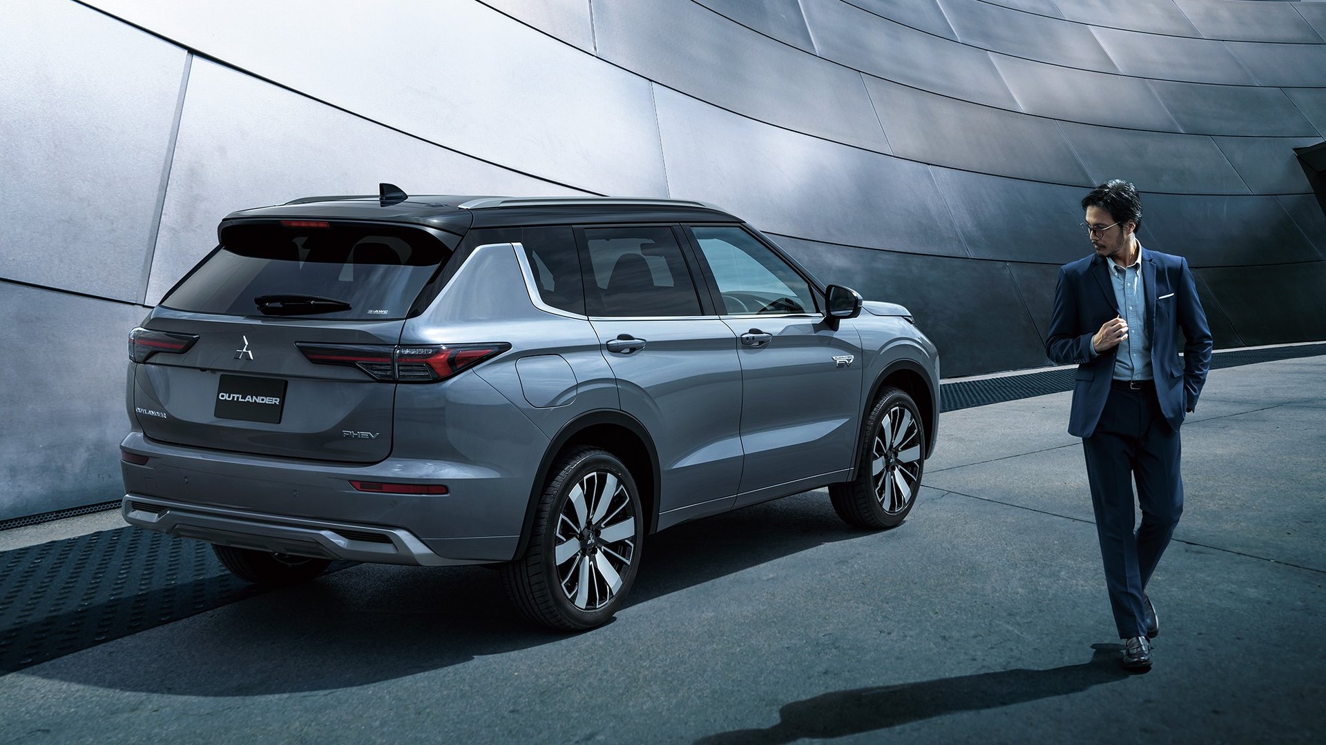 Mitsubishi Outlander PHEV prateado visto de trás e três quartos, com uma pessoa a passar ao lado