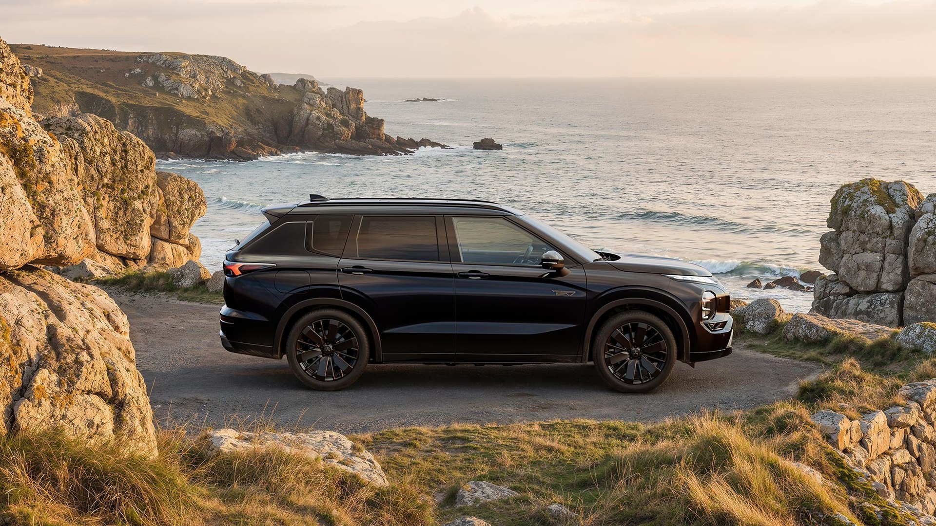 Mitsubishi Outlander PHEV preto de perfil, num miradouro sobre o mar ao fim da tarde