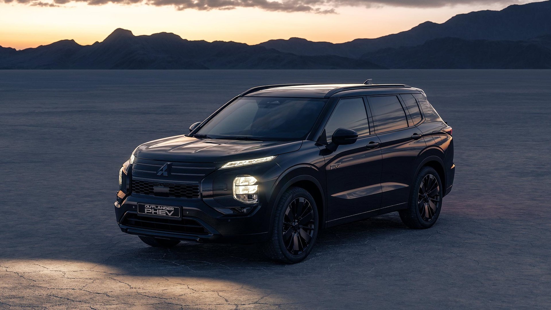 Mitsubishi Outlander PHEV preto, de frente e três quartos, num deserto de sal ao pôr do sol