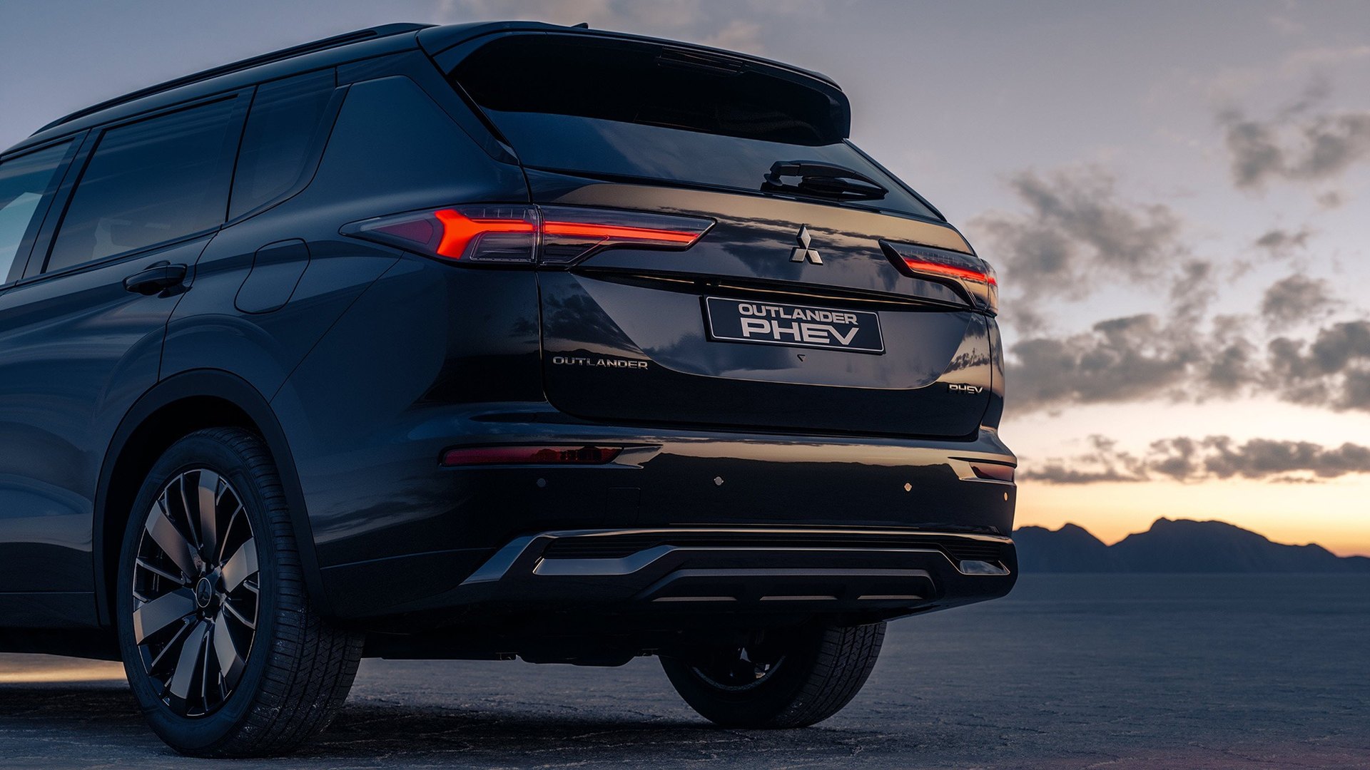 A traseira de um Mitsubishi Outlander PHEV preto, com o farolim aceso ao anoitecer